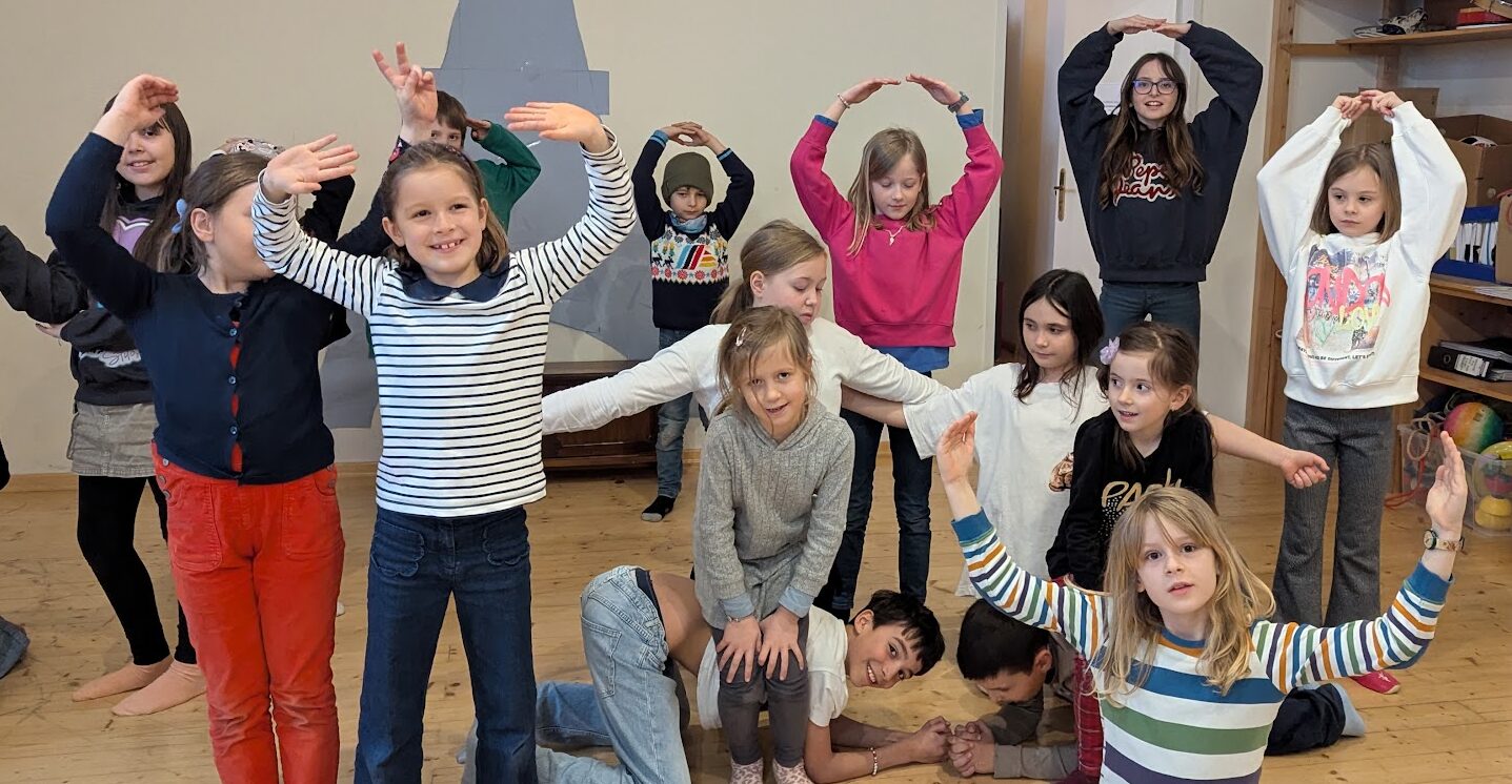 Kinder sitzen und stehen und stellen gemeinsam eine Maschine dar.